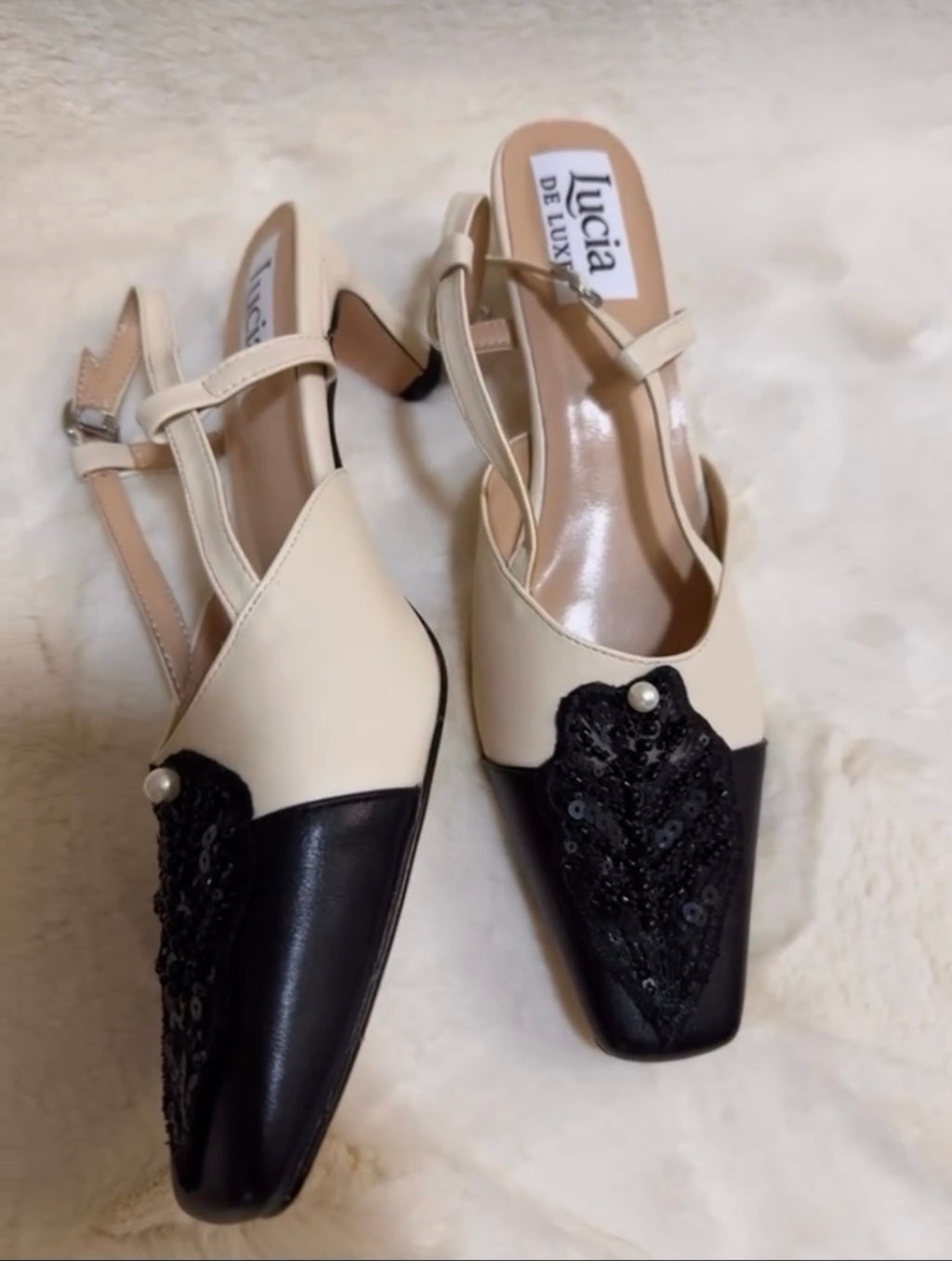 Pair of black and white high-heeled shoes with lace details on a light background