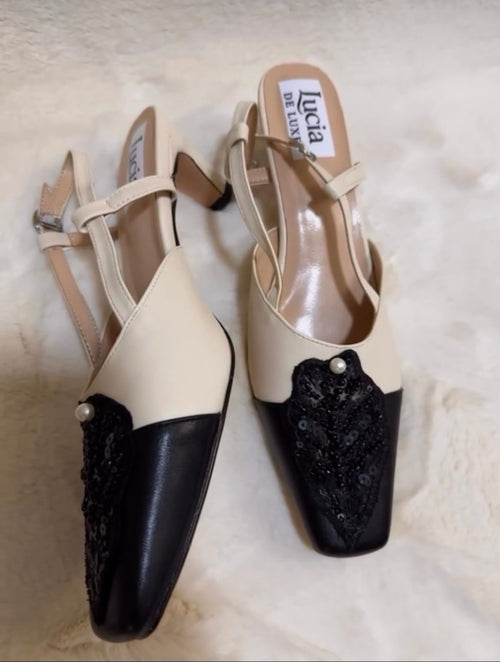 Pair of black and white high-heeled shoes with lace details on a light background